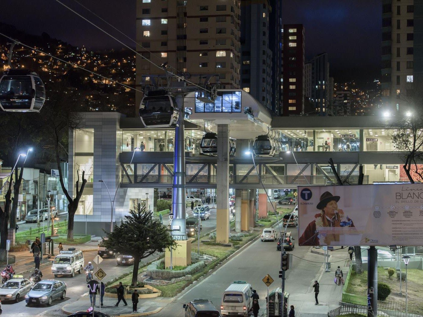 Night view of a La Paz Mi Teleférico station: cabins leaving the illuminated station, with the city lights beyond