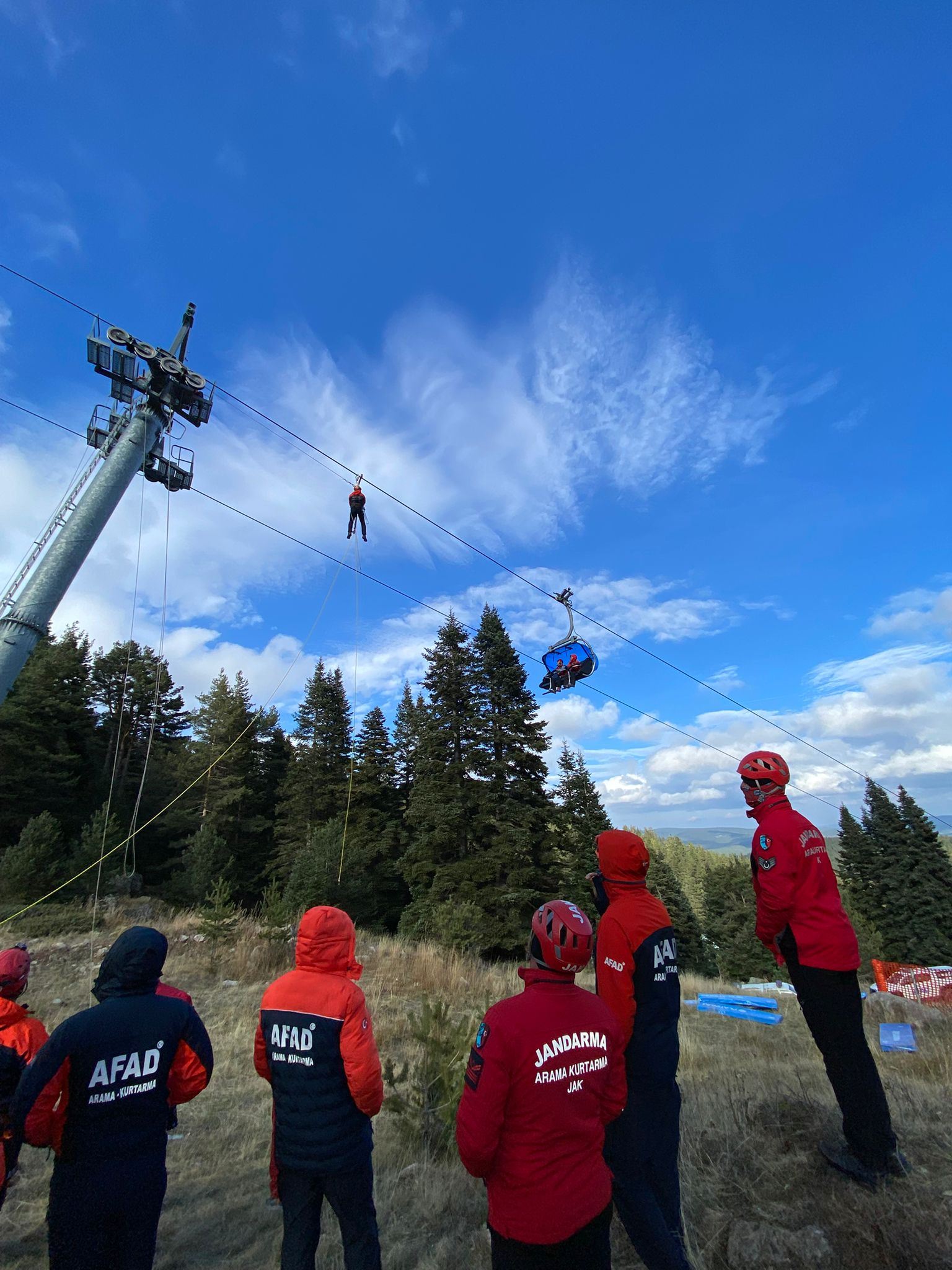 A rescuer moving along the track rope towards a suspended carrier while teams watch from the ground