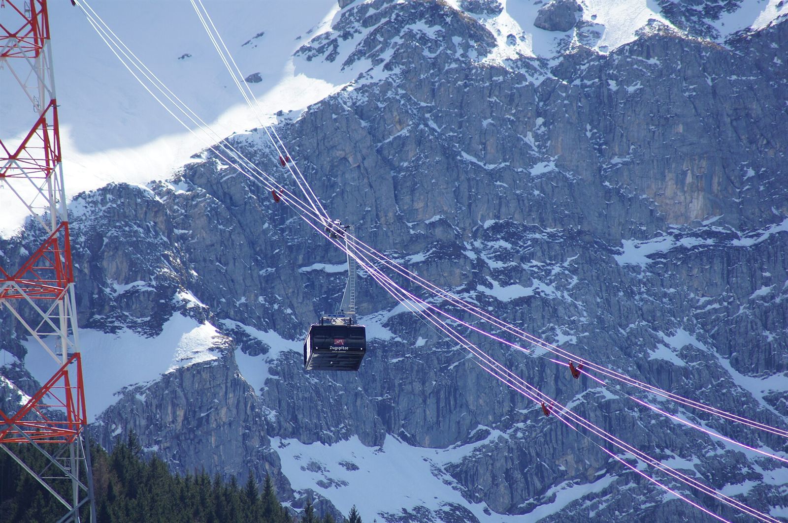 Cabin suspended from ropes in front of the Zugspitze rock face, with a red and white steel tower